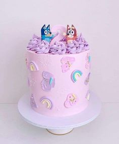 there is a pink cake with purple frosting on the top and two small figurines in the middle