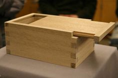 a small wooden box sitting on top of a white cloth covered table with people in the background