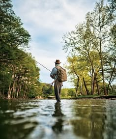 a man standing in the middle of a river holding a fishing pole and a bag