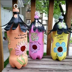 three painted water bottles sitting on top of a wooden table next to each other in front of a house