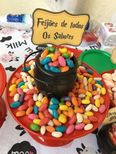 there is a red bowl filled with candy on top of a table that has other candies in it