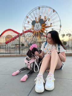 a woman sitting on the ground with her dog in front of an amusement park ferris wheel