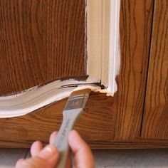 someone using a paint brush to paint the trim on a wooden cabinet door with brown stain