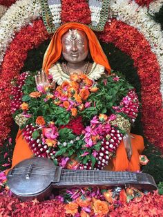 a statue of a person sitting in front of flowers and an instrument on the ground