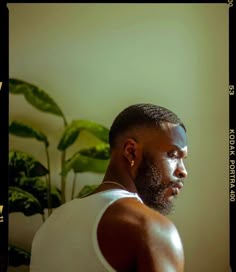 a man in white tank top looking off into the distance with green plant behind him