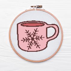 a cross stitch coffee mug with a snowflake on it is hanging from a hoop