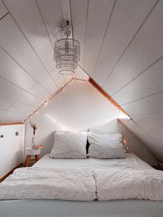 a bed with white sheets and pillows in a room that has lights on the ceiling