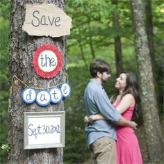 a man and woman standing next to each other in front of a tree with a save the date sign on it