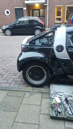 a car that is sitting on the side of the road with its door open and some tools in front of it