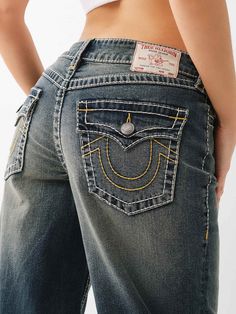 The Bobbi Big T Baggy Jean features a low-rise waist, zip fly, subtle fading, wide leg, and two-tone Big T stitching. Finished with horseshoe detailing on the back flap pockets and burnished hardware.    Style: 208451 Straight Jeans And Heels, Baggy Ed Hardy Jeans, 90s Jeans Women, Real 1980s Fashion, Where To Buy Low Rise Baggy Jeans, Ed Hardy Baggy Jeans, Denim Skirt Outfits Fall, Levi Baggy Jeans, Cotton On Jeans