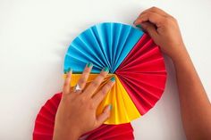 a person holding a colorful fan on top of a white wall next to a pair of hands