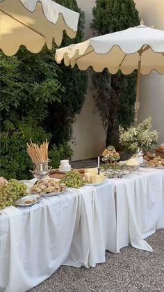 an outdoor buffet with grapes, cheese and bread on the table under two umbrellas