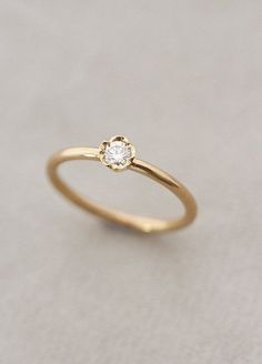 a gold ring with a single diamond on the top, sitting on a white surface