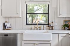 a kitchen with white cabinets and an open window above the sink is decorated with gold faucets