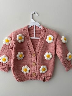 a pink sweater with white and yellow flowers is hanging on the wall next to a hanger