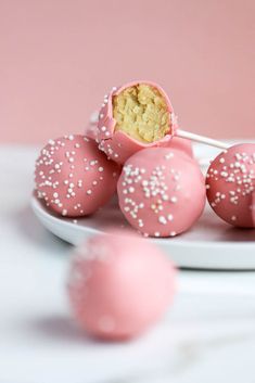 pink cake pops with white sprinkles on a plate next to some cookies