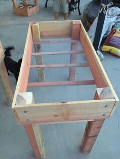 a black dog standing next to a wooden bed frame on the ground with two people looking at it