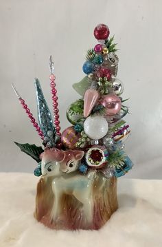 a small christmas tree with ornaments on it's top and an animal figurine in the middle