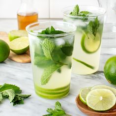 two glasses filled with mojita tea and limes on a marble counter top