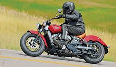 a person on a red motorcycle driving down the road with grass in the back ground