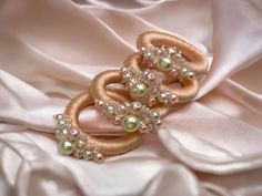 two brooches are sitting on a pink satin material with pearls and beads in the middle