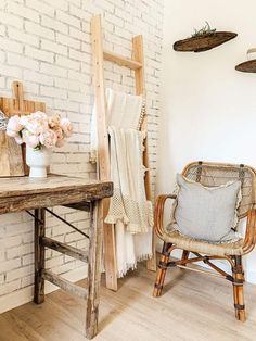 a chair sitting in front of a wooden table next to a white brick wall with hanging baskets on it