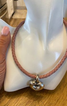 a woman's hand holding onto a brown leather bracelet with a silver heart charm