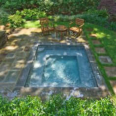 an outdoor hot tub in the middle of a garden with two chairs and tables around it