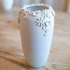 a white vase sitting on top of a wooden table next to a cell phone and cup