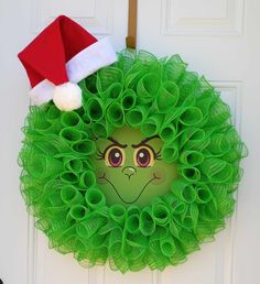 a green wreath with a face drawn on it and a santa hat hanging from the front door