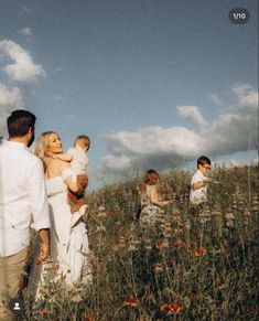 a group of people standing in a field with one woman holding a baby and the other man holding a toddler