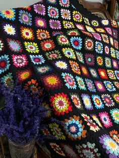 a crocheted blanket is on a bed with purple flowers in the corner and a potted plant next to it