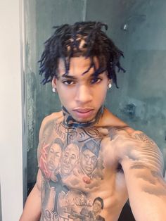 a man with dreadlocks and tattoos on his chest standing in front of a mirror