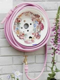 a pink garden hose attached to a white brick wall with flowers in the foreground