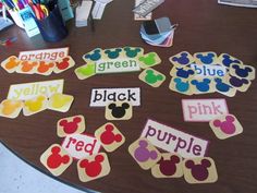 mickey mouse name tags on a table with other items in the room behind them that say orange, green, yellow, pink, and purple