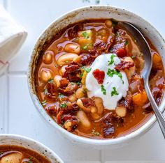 two bowls of chili and beans soup with sour cream on top, sitting next to each other