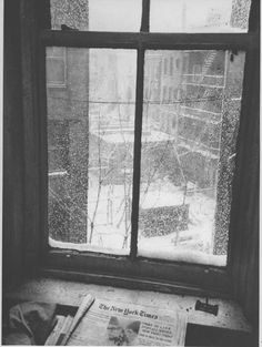 an old window with snow falling on the windowsill and newspaper laying next to it