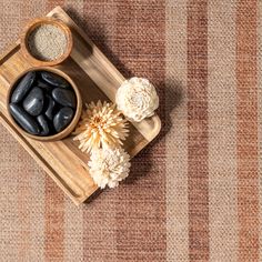 a wooden tray topped with black stones and white flowers on top of a carpeted floor