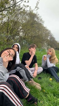 four people sitting in the grass with their eyes closed and one person covering his mouth