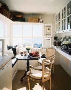 a small table with two chairs in front of a window and some books on the shelf