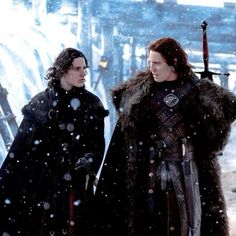 two men dressed in black standing next to each other with swords on their shoulders and wearing fur coats