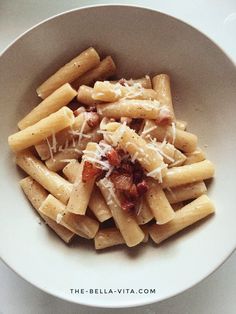 pasta with bacon and parmesan cheese in a white bowl on a table top