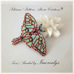 a beaded butterfly brooch sitting on top of a white flower next to it