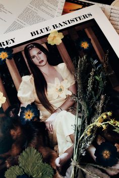 a woman sitting on top of a magazine next to flowers