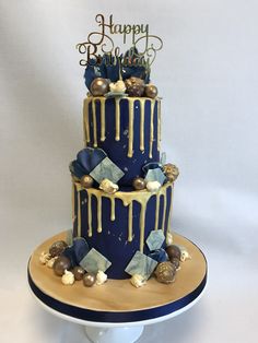 a three tiered blue and gold birthday cake with white icing dripping down the side