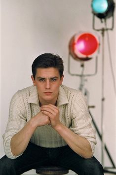 a young man sitting on top of a stool in front of a red light bulb