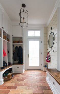 an entryway with white cabinets and red tile flooring, along with a wooden bench on the other side