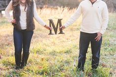 a man and woman holding the letter m while standing next to each other in a field