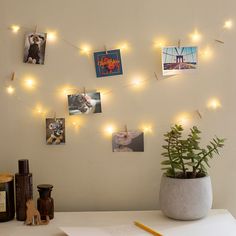 a white table topped with pictures and lights next to a pot filled with plants on top of it