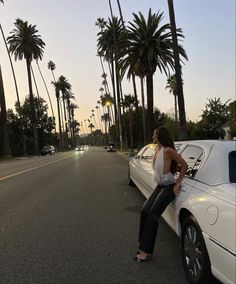 a woman sitting on the hood of a white car in front of some palm trees